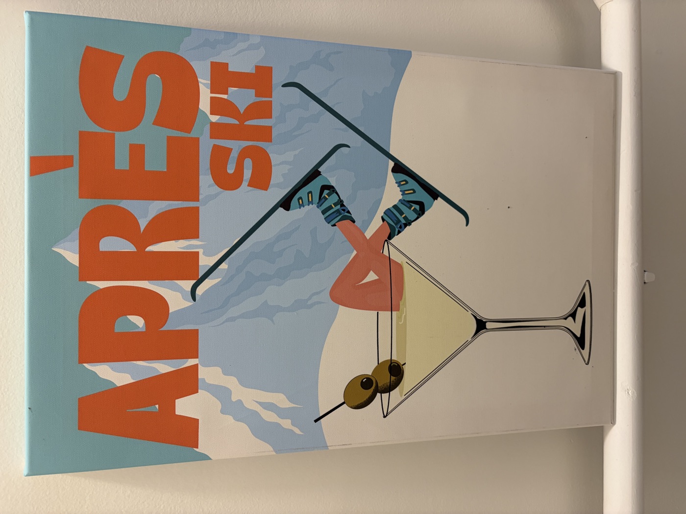 An Après Ski print: a skier's legs and boots kicking out of a giant martini glass, mountains behind.