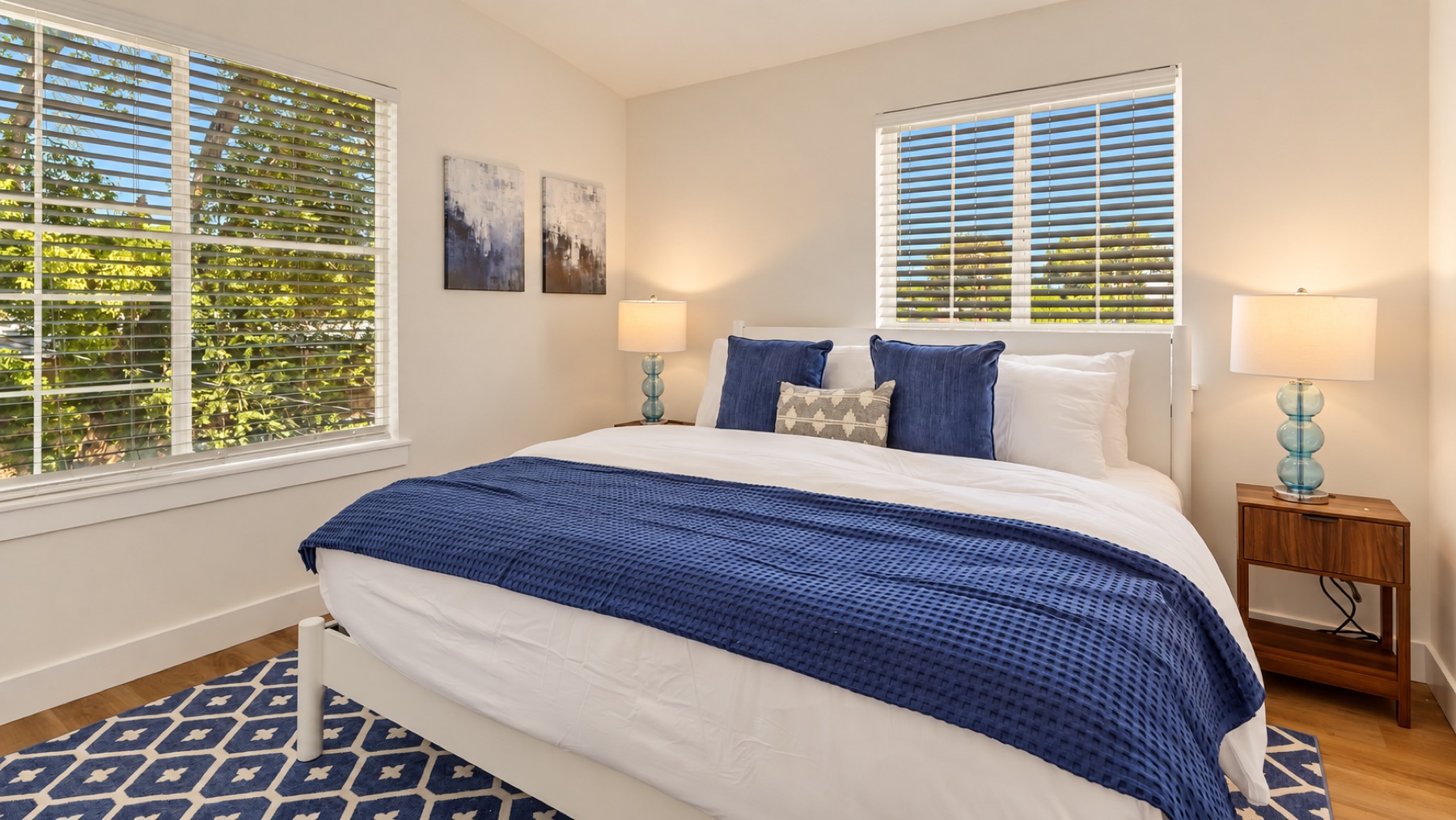 The primary bedroom: a white bed with a navy throw, two lamps, and the trellis rug underneath.
