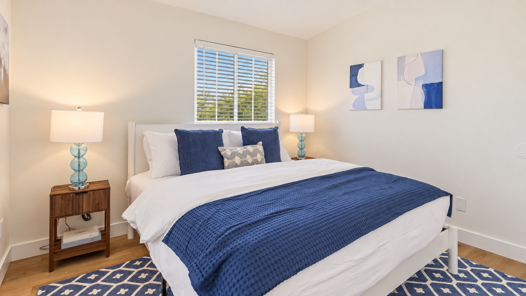 Bedroom two: navy bedding, two blue-glass lamps, and a pair of blue abstracts over the bed.