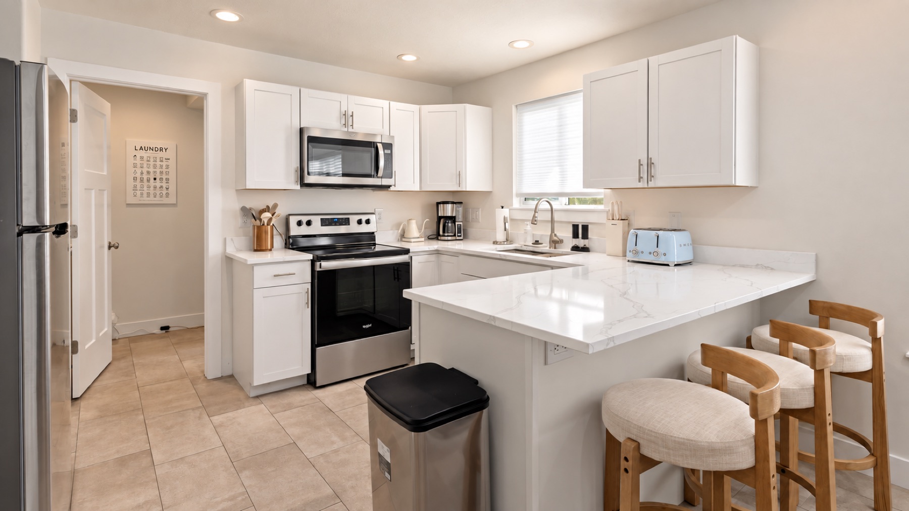 The kitchen: white cabinets, a stainless range and microwave, and a breakfast bar with three stools.