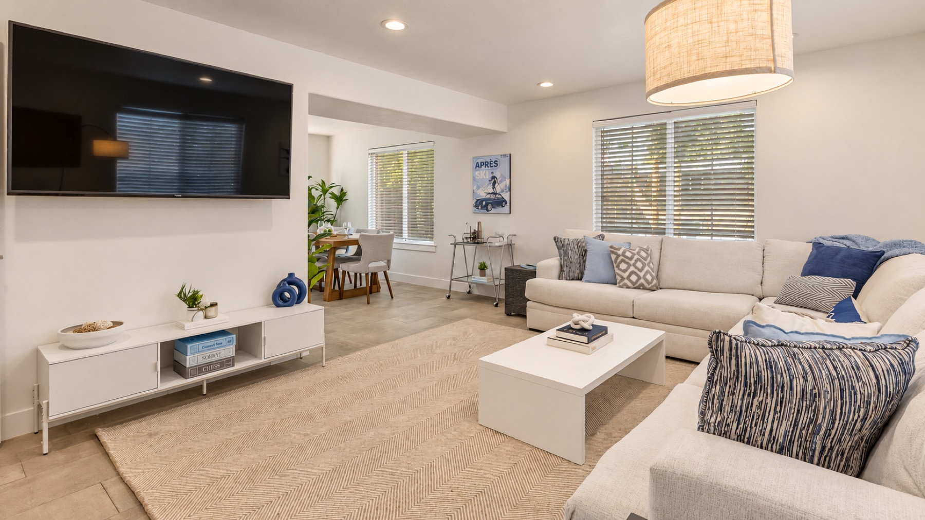 Summit's living room: a cream sectional in navy and blue, the TV wall, and the dining table beyond the arch.