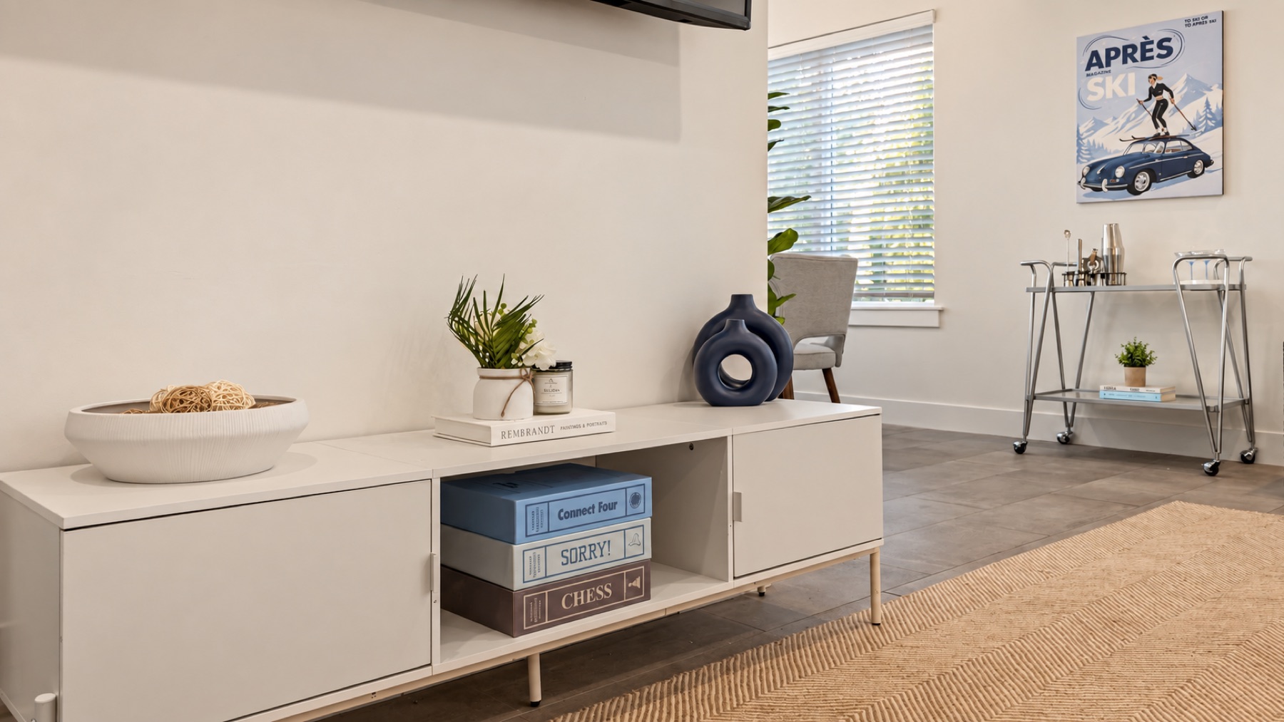 The console under the TV: a woven bowl, a blue vase, and the board games stacked where guests can find them.