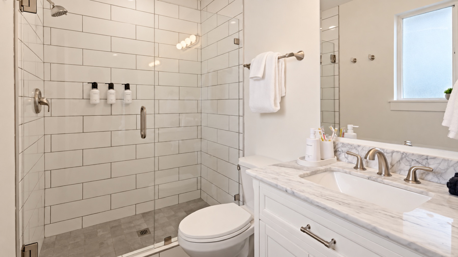 The primary's own bath: a walk-in glass shower in white subway tile and a marble vanity.