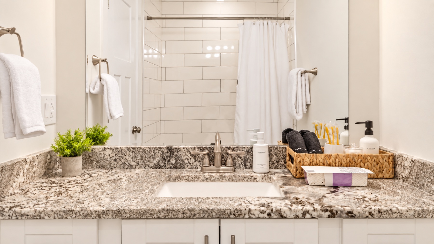 The shared bath for bedrooms two and three: a granite vanity, fresh towels, and the tub behind the curtain.