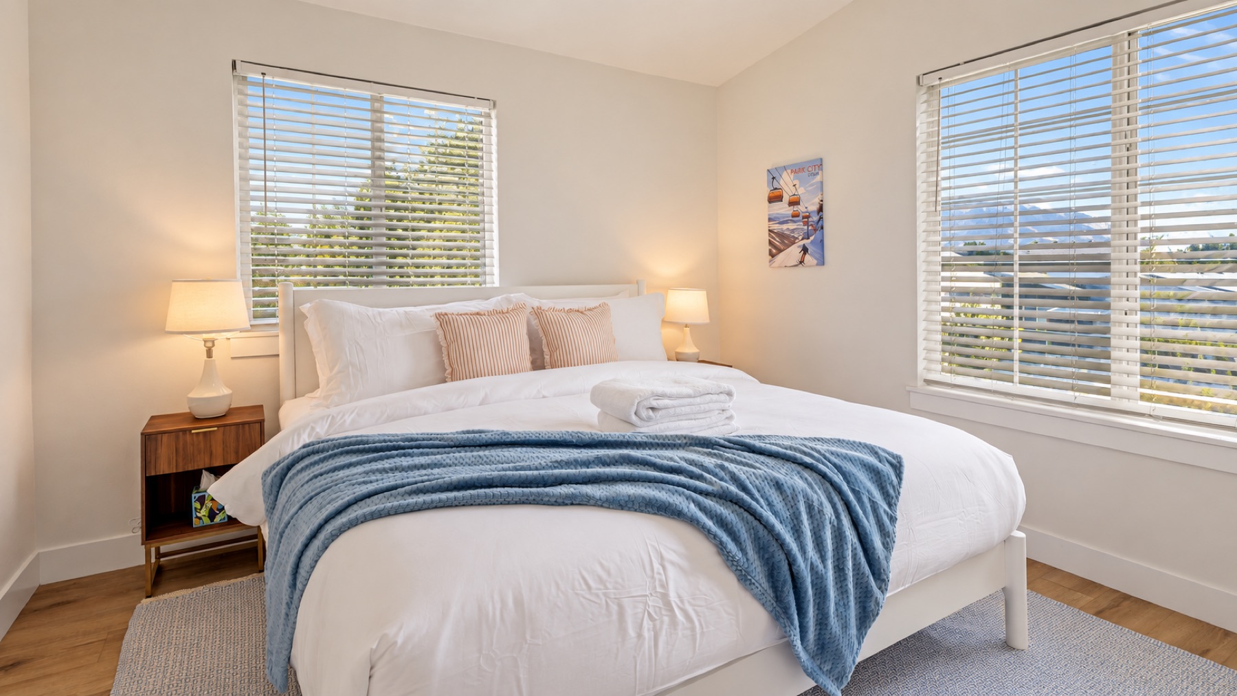 Bedroom two: a white bed with a blue throw between two windows, a gondola print on the wall, and the range in the window.