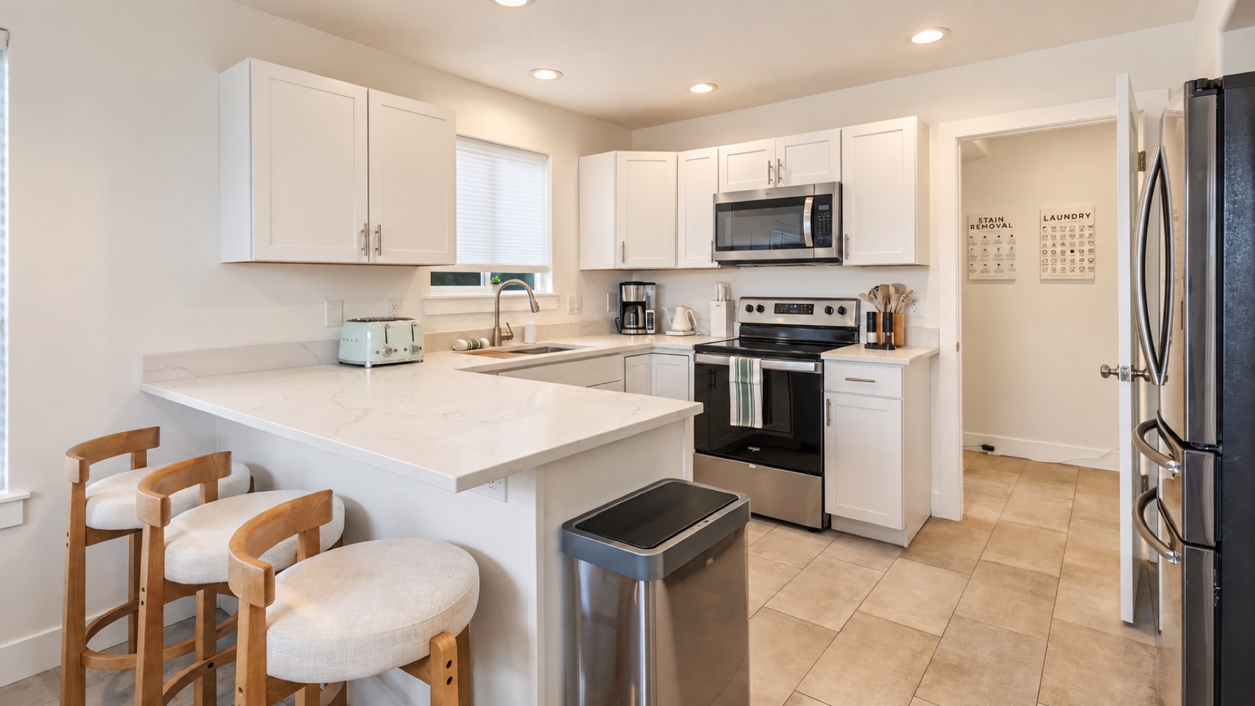 A full kitchen: white cabinets, quartz counters, a stainless range and fridge, and a breakfast bar with stools for the early risers.