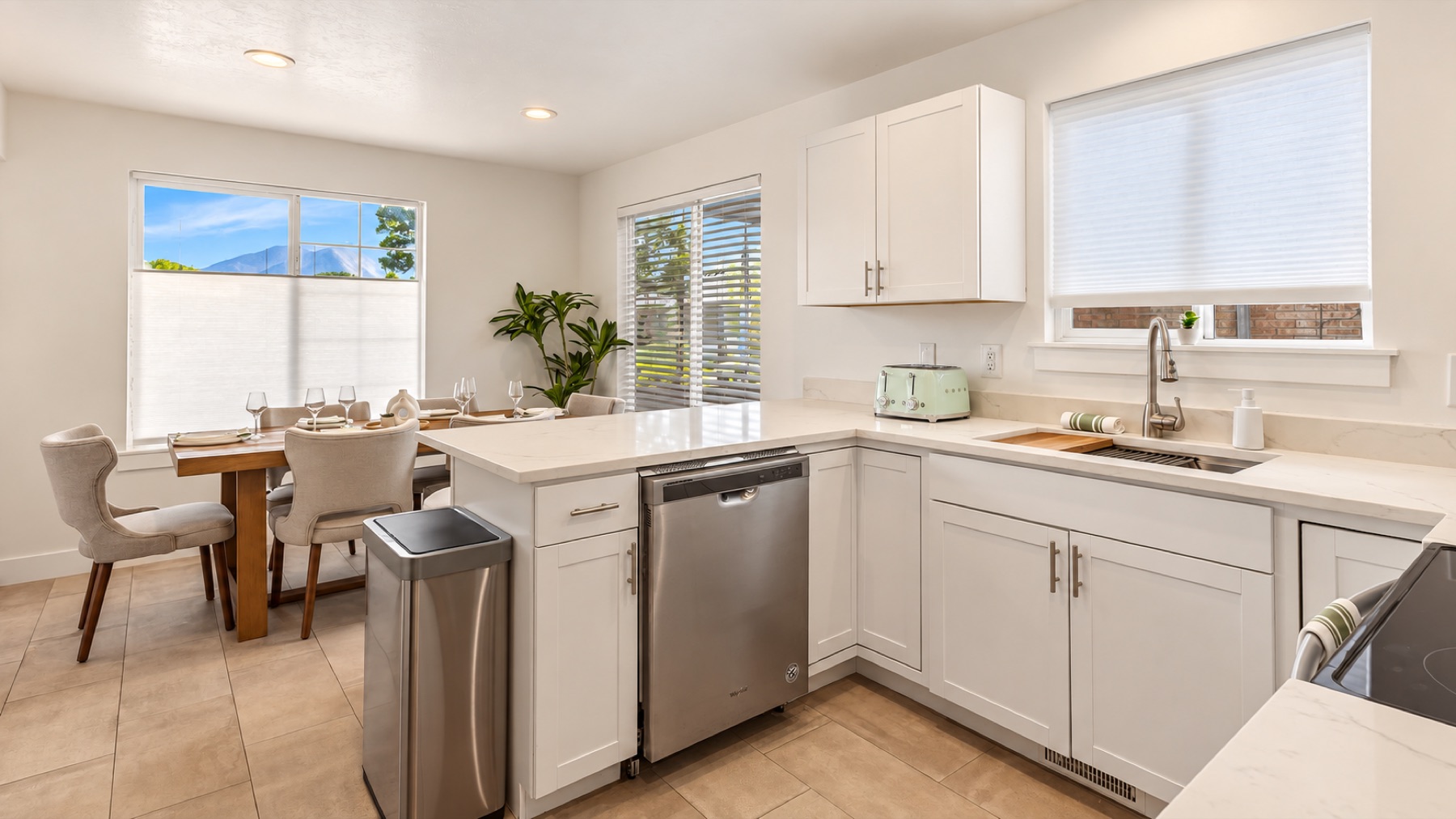 The kitchen from the counter: white cabinets, a stainless range, and mountains through the windows over the sink and the table.