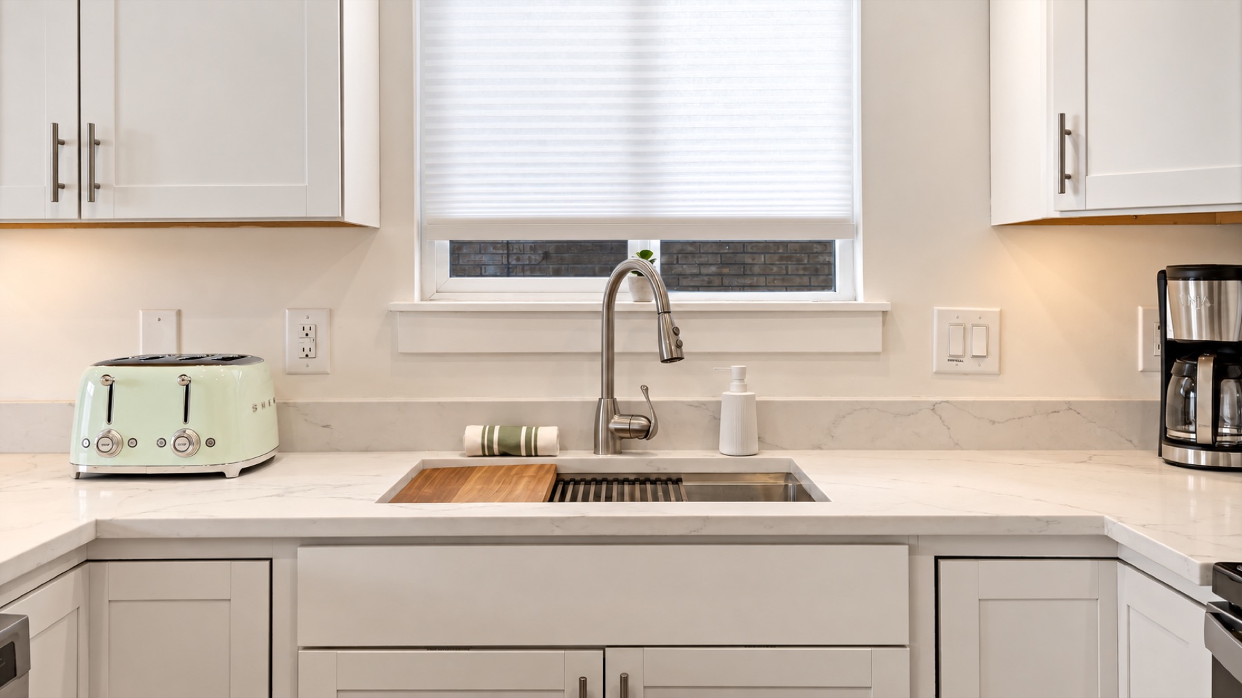 The sink window, a mint toaster, and a coffee maker that is on before you are.