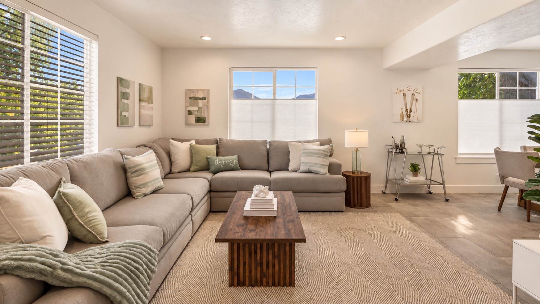 Timberline's front room: a deep grey sectional with sage pillows, a walnut coffee table, and the Wasatch mountains showing through the front windows.