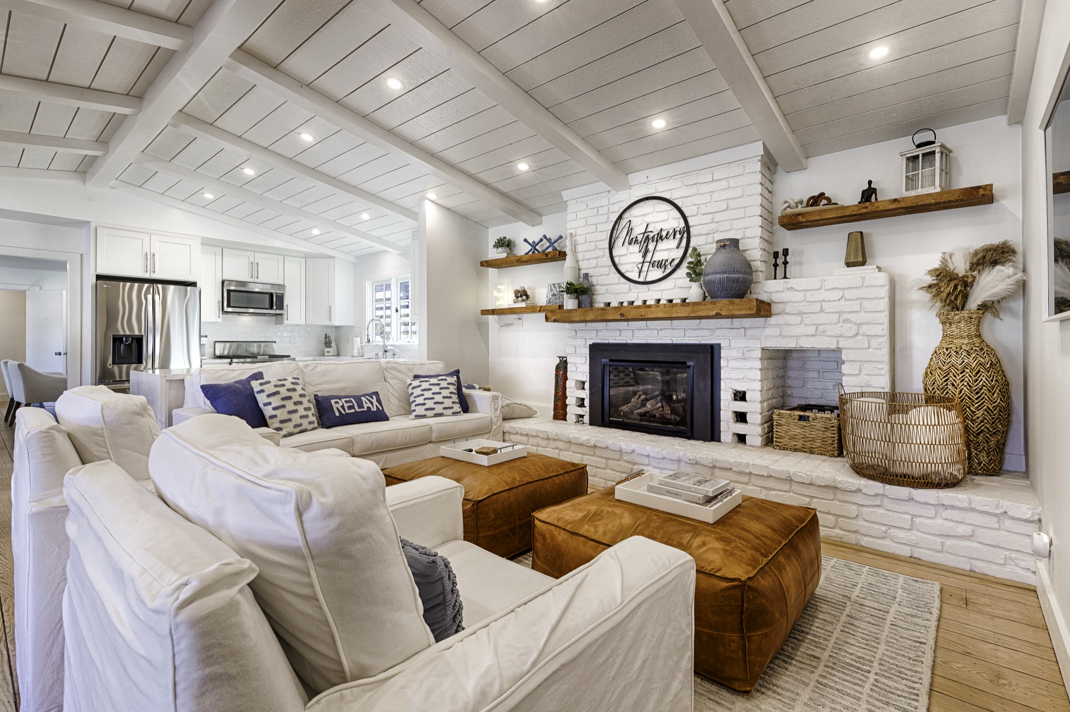 The Montgomery House living room — whitewashed brick fireplace, slipcovered sofas, leather ottomans